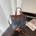 Blaue Denim-Beuteltasche mit braunen Ledergriffen und Goldnieten auf einem Schreibtisch - Blau Denim Braun Splicing