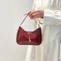 Glanzende bordeauxrode hobo tas met gouden gesp over de schouder op een witte wand - Rood
