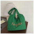 Nahaufnahme einer grünen Plissee-Stofftasche mit orangefarbenem Fanyissa-Text auf Holz - Hellgrün