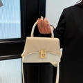 Elegant cream leather patchwork handbag with gold oval lock held against black outfit - White