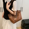 Minimalist brown faux leather tote bag with lychee texture shown on shoulder - Brown