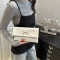 Elegant white leather envelope bag with a golden metal bow fastener held by hand - White