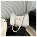 Close-up of white crocodile texture leather underarm bag with gold bow clasp detail - White