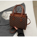 Detail view of brown monogram crossbody bag with gold text on grey blazer background - Coffee