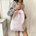 Light pink backpack featuring cartoon cat patterns and blue bows with a zipper front pocket - Pink