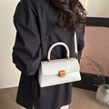 Elegant cream leather square handbag with golden clasp shown on a shoulder - White