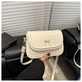 Close-up of cream flap crossbody bag featuring a delicate gold bow metal hardware detail - White