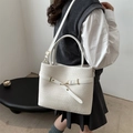 White faux crocodile tote bag with metal buckle and shoulder strap worn by a model - White