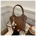 Detail of a brown bucket bag with a plush charm and detachable strap in a cozy setting - With Pendant Style / Brown