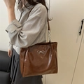 Detail of dark brown tote bag with glossy finish and silver bow accent on model - Brown