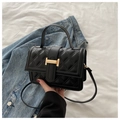Detalle de bolso bandolera acolchado negro con hebilla dorada en H sobre fondo denim - Negro