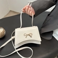 Bolso de mano elegante crema con lazo dorado y base curva mostrado en la mano - Blanco