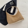 Detail of hand-woven straw hobo bag with white leather straps on a blue blazer background - White