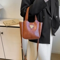 Braune Vintage-Eimertasche aus Leder mit goldenem Dreieckslogo an einem Model - Braun Ohne Anhänger