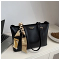 Detalle de bolso tote de cuero negro con pañuelo de seda y letras doradas en mesa blanca - Negro