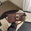 Brown leather crossbody bag with gold woven buckle and knot strap on a beige knit rug - Brown