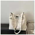 Close-up of ivory tote bag with functional pockets and black drawstring closure on sofa - Off White