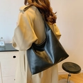 Minimalist black large capacity leather tote bag worn by a model in a beige coat - Black