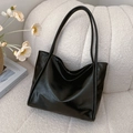 Minimalist black faux leather tote bag with slender straps on a white sofa - Black