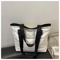 Close-up of silver quilted tote bag featuring black woven handles and puffer fabric detail - White