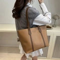 Bolso tote grande de cuero caqui con adornos marrones y correas de hombro en la modelo - Tostado