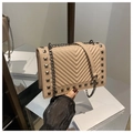 Macro detail of beige quilted leather bag with V-shaped stitching and dark metal rivets - Khaki