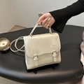 Retro cream-colored square crossbody bag with dual buckle design on a sleek pedestal - Off White