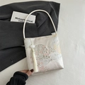 Sac seau en satin beige avec broderie florale et pompon blanc dans un cadre épuré - Blanc