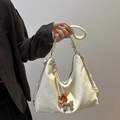Cremeweiße Hobo-Tasche mit silbernem Schleifenanhänger und Bernsteinperlen in der Hand - Weiß