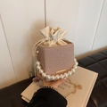 Summer woven bucket bag with pearl handle and gold chain strap on a white book - Khaki