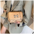 Detail of beige quilted crossbody bag featuring silver bow and gold metal trim edge - Khaki