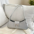 Metallic silver underarm bag with a metal bow buckle on a soft white sofa setting - Silver