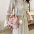 Pink drawstring bucket bag with metal chain detail and white pom-pom charm on model - Pink (With Glasses Pendant)