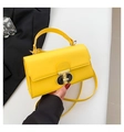 Detail of a bright yellow crossbody square bag featuring a unique gold and black lock - Yellow