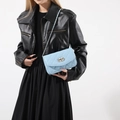 Sky blue quilted crossbody bag with silver chain strap shown on black outfit - Blue