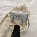 Detalle de bolso bandolera azul y blanco con lazo plateado sobre blazer claro - Azul y Blanco