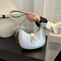 Sleek silver crescent shoulder bag with gold metallic buckle closure held by hand - Silver