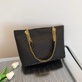Black tote bag with geometric star texture and gold chain straps on metallic surface - Black