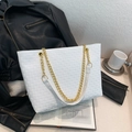 White woven tote bag with gold chain strap placed on a stylish black leather jacket - White