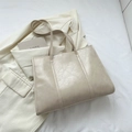Minimalist beige tote bag with cracked leather texture shown in a clean lifestyle setting - Beige
