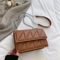 Brown quilted crossbody bag with geometric pattern and silver chain strap on white bed - Brown
