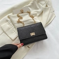 Black quilted crossbody bag with gold chain strap and turn-lock closure on white blazer - Black