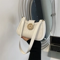 White quilted underarm bag with gold ship wheel buckle held by a model in a modern room - White