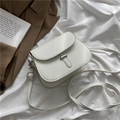 Minimalistische weiße Kunstleder-Satteltasche mit silbernem Schloss auf Bett - Weiß