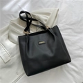 Minimalist black faux leather tote bag with gold fashion tag on white blazer - Black
