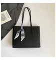 Detail of black pebbled leather tote bag with a floral silk scarf on a gray suit background - Black
