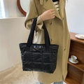 Borsa tote nera trapuntata con tracolla larga indossata da una modella in interno - Nero