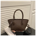 Detalle de bolso cubo en cuero marrón oscuro con asas y accesorios metálicos plateados - café