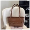 Détail d'un sac à bandoulière en cuir marron avec boucle décorative sur chaise blanche - Fauve