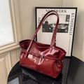 Large dark red patent leather tote bag with silver buckle on a sleek black table - Red